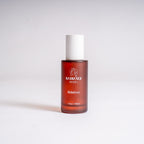 A 2 fl oz amber glass bottle of RebelMist by Radiance Rebel with a white cap, standing upright on a light gray background.