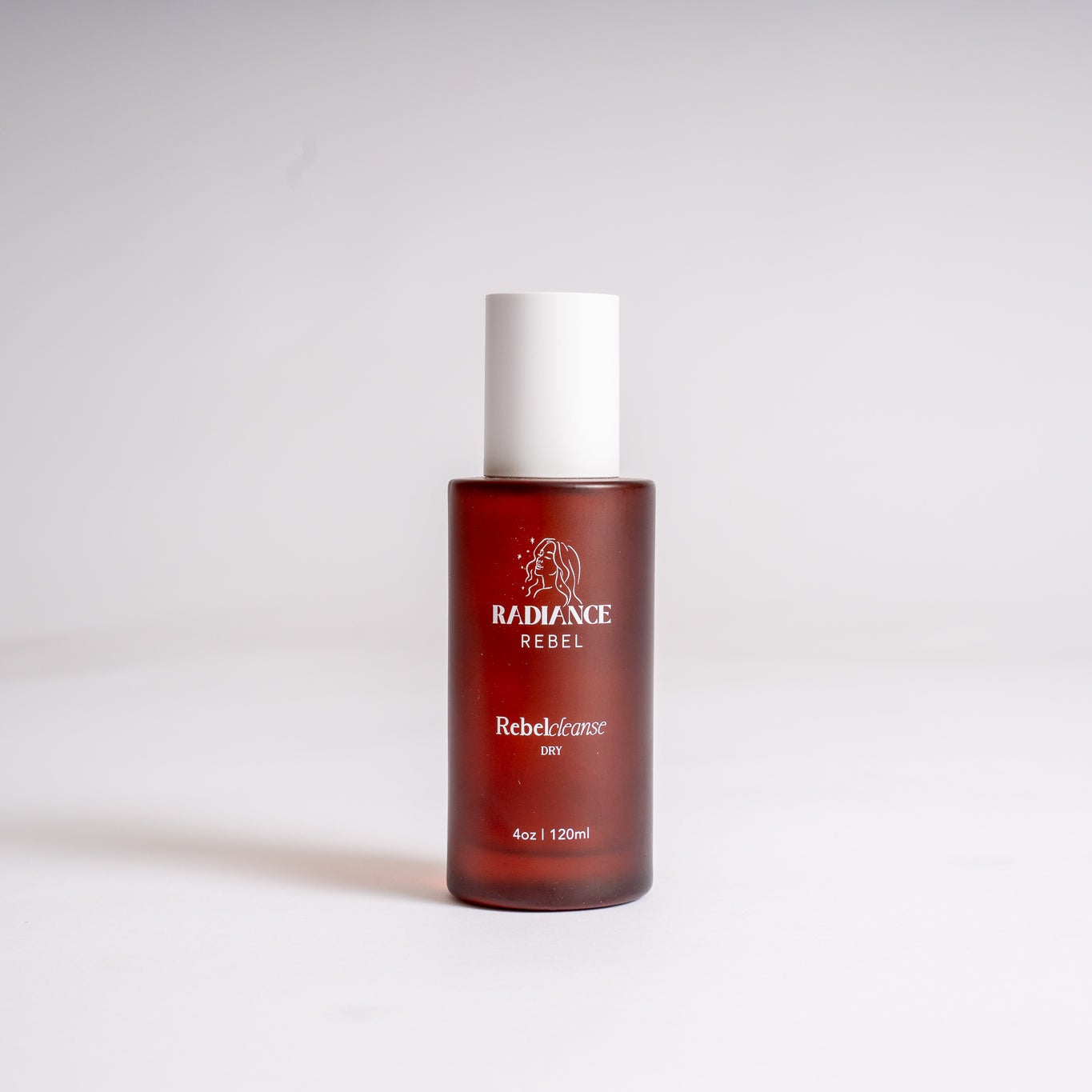 A bottle of RADIANCE REBEL RebelCleanse Dry cleanser, featuring a translucent amber-brown bottle and a white cap, set against a plain light gray background.